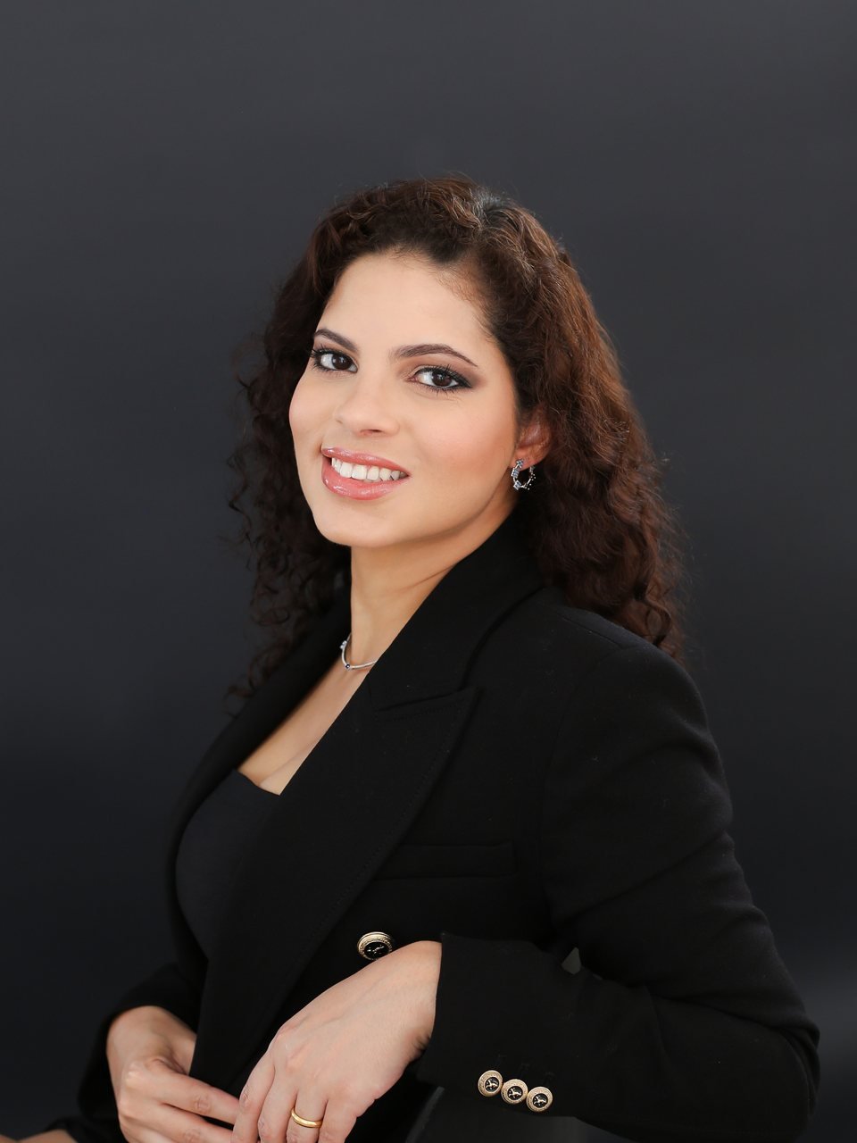 Retrato da Dra. Thaíza Andrade de blazer preto, sorrindo, sobre fundo escuro.